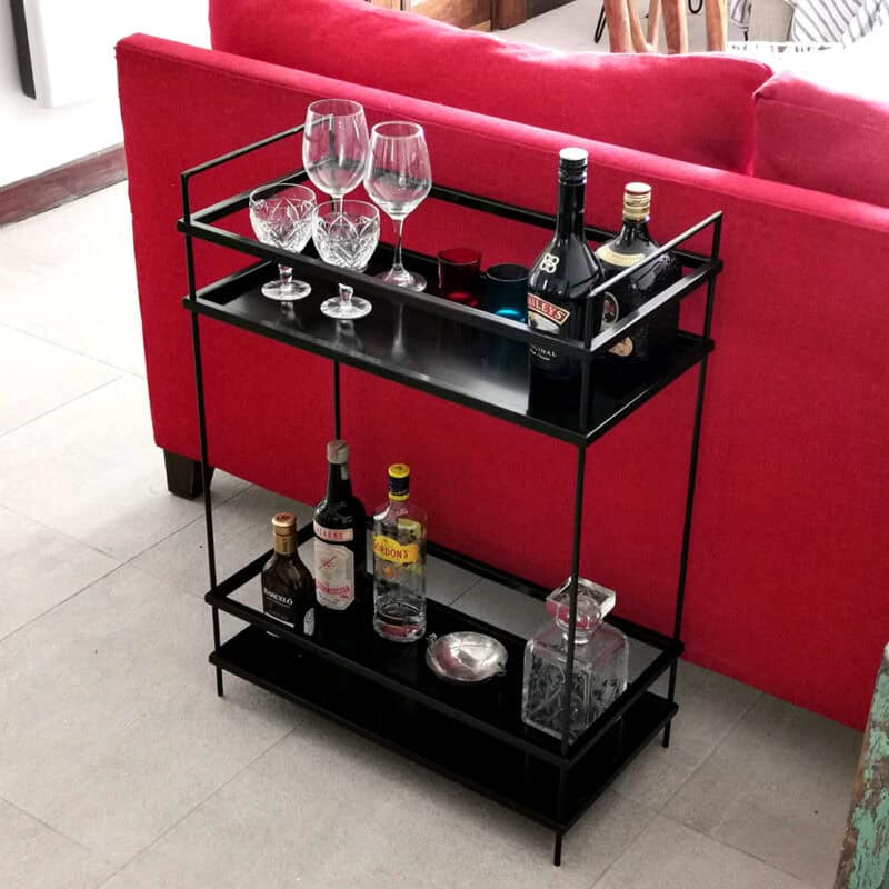 Carrito de bar negro con bebidas y copas en sala moderna.